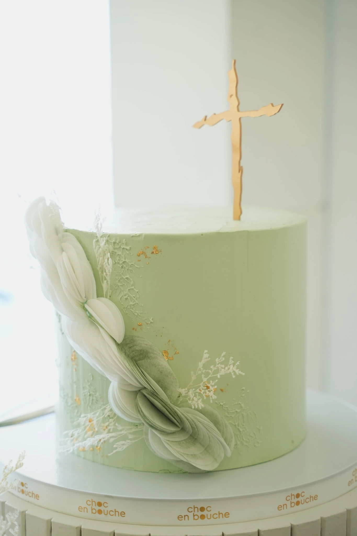 Gâteau de baptême vert pâle, fleurs en sucre et croix dorée