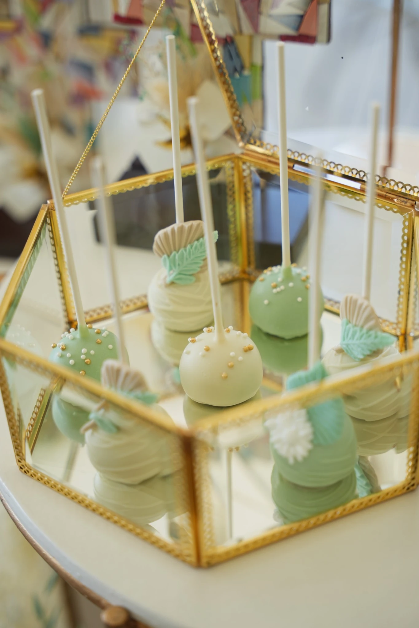 Cake pops de baptême vert menthe et ivoire présentés dans une vitrine dorée